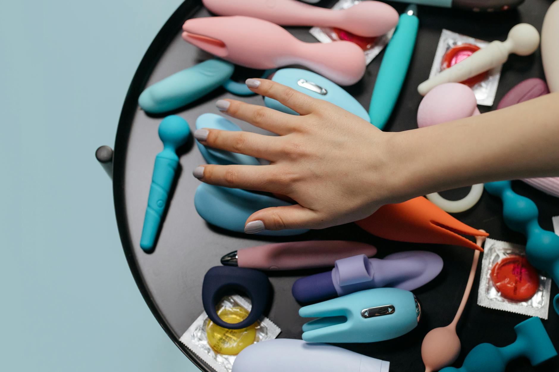 Due mani che tengono vibratori in silicone rosa e blu su sfondo color pastello