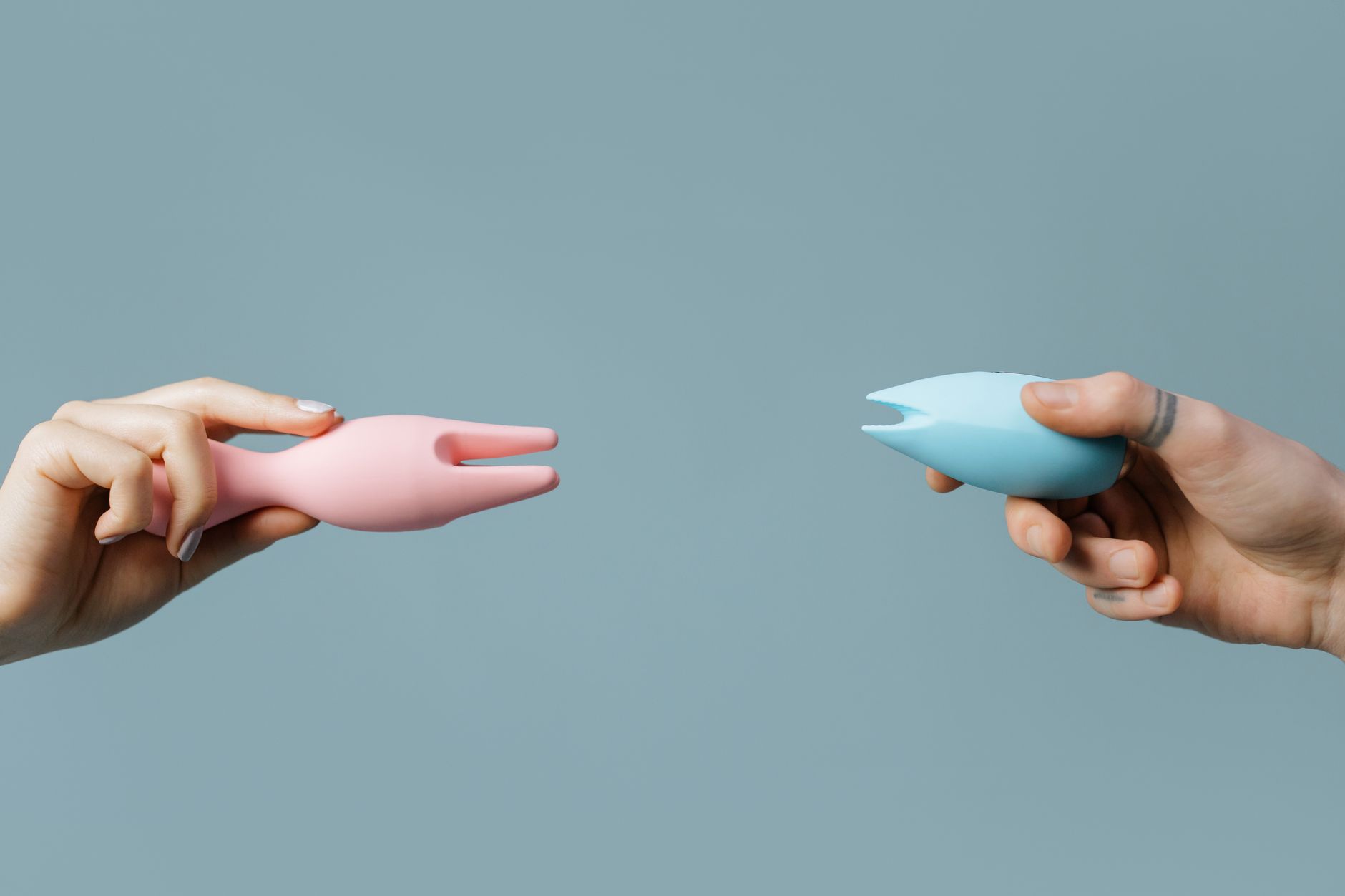 Due mani che tengono vibratori in silicone rosa e blu su uno sfondo pastello