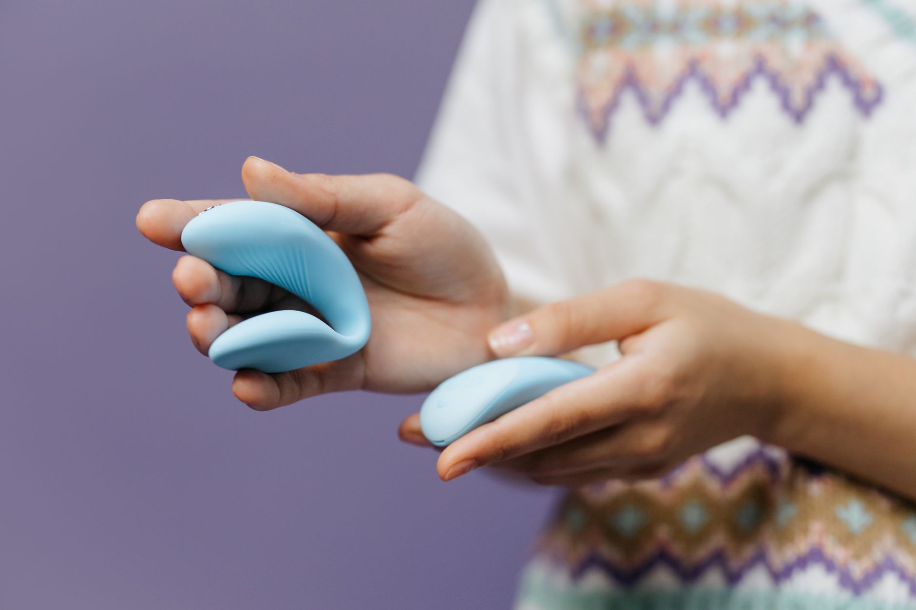 Mani che tengono un elegante vibratore blu contro uno sfondo viola, simboleggiando l'auto-esplorazione consapevole.