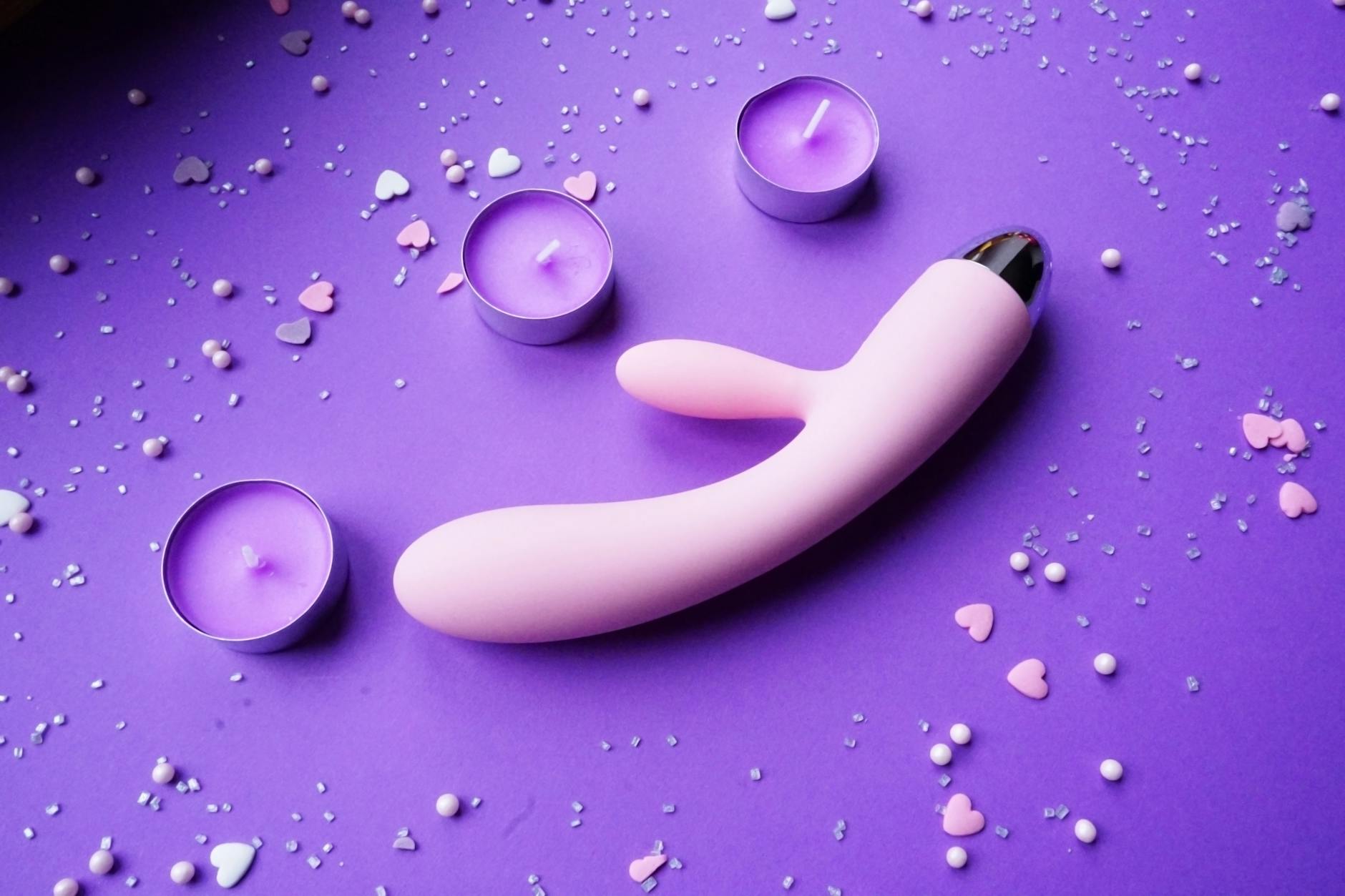 Vibratore rosa su sfondo viola con coriandoli a forma di cuore e candele per un'atmosfera romantica